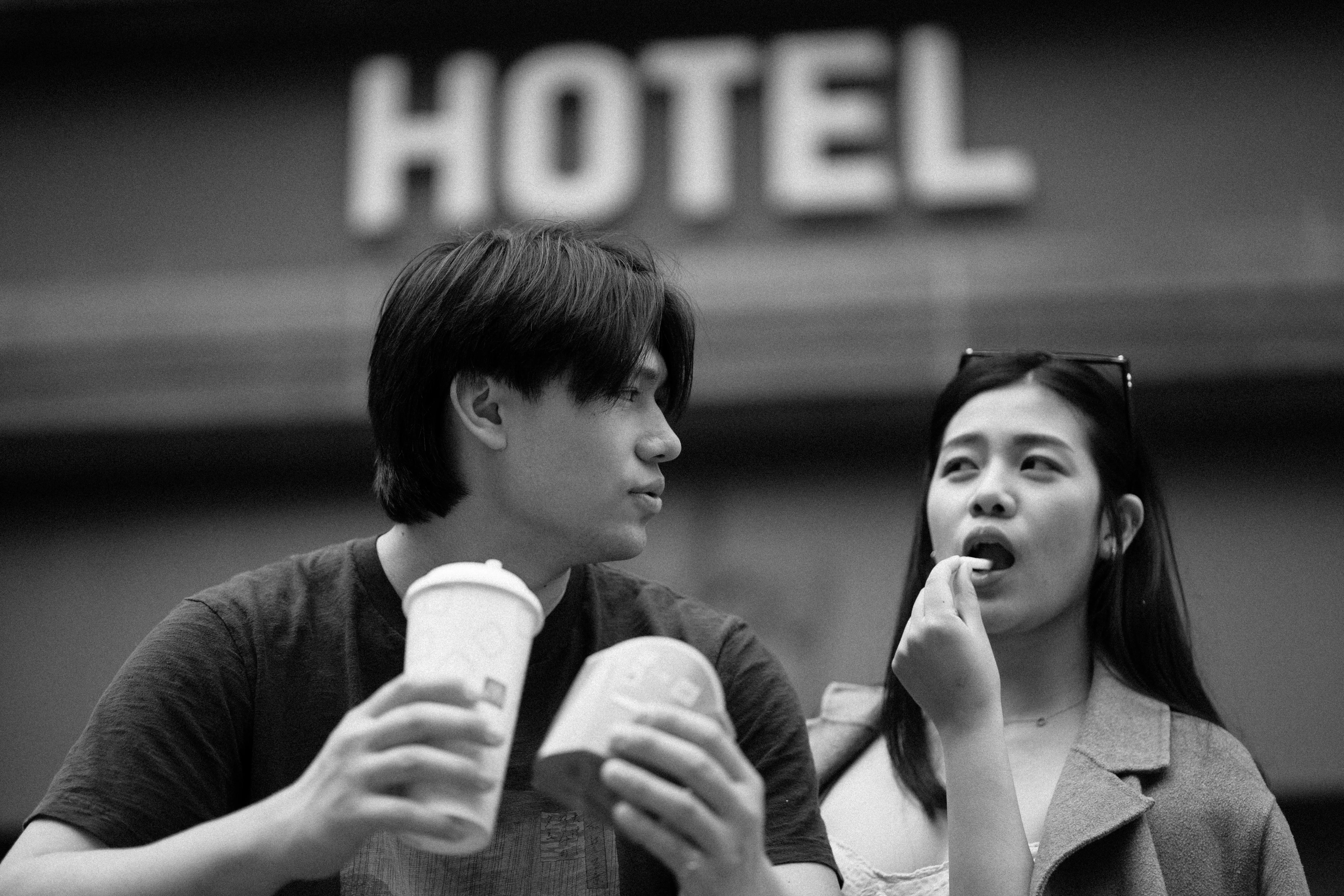 A couple sharing food beneath a hotel sign in a monochrome photograph